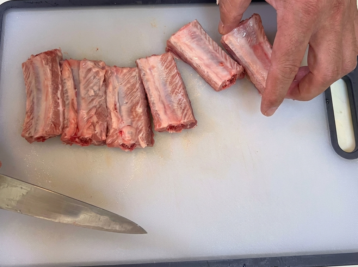 Un cuchillo retirando la membrana fina del lado interno de las costillas de cerdo crudas.