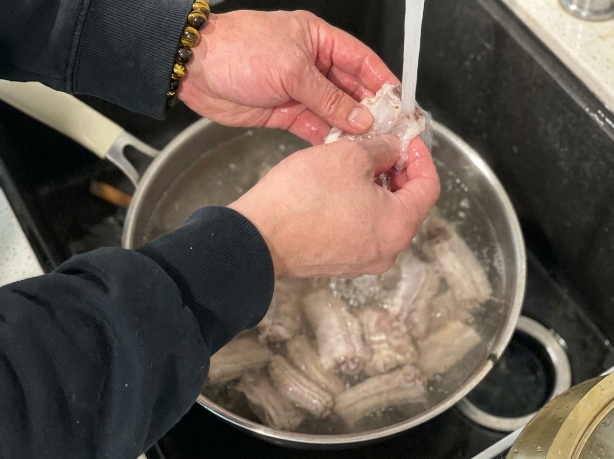 Costillas de cerdo escaldadas enjuagándose bajo el grifo de agua fría.