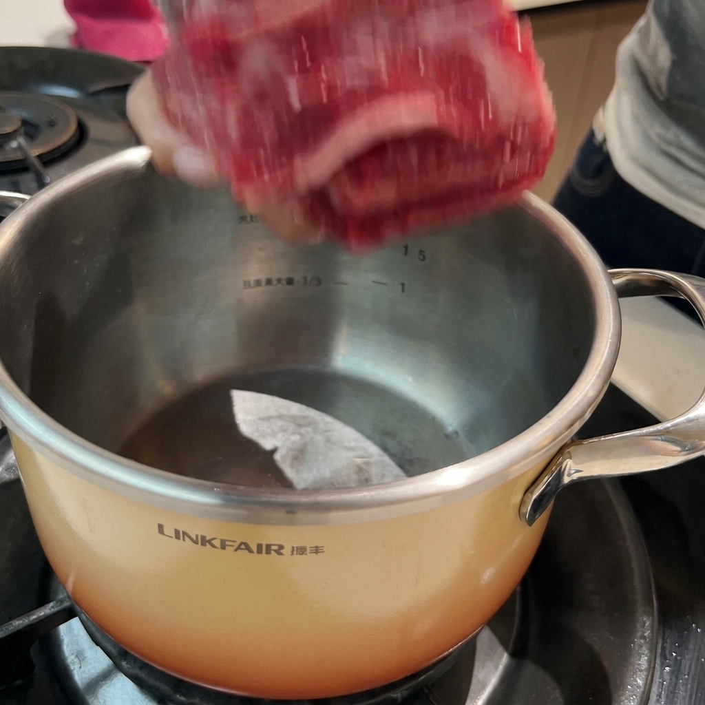 Costillas de res remojando en una olla con agua fría y aromáticos para el proceso de escaldado.