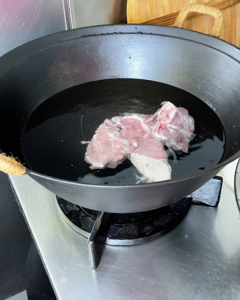 Espinazo de cerdo en un wok con agua fría, jengibre, cebollinos y vino para cocinar.
