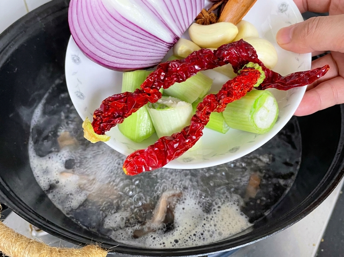 Espinazo de cerdo en un wok con aromáticos y agua hirviendo siendo vertida.