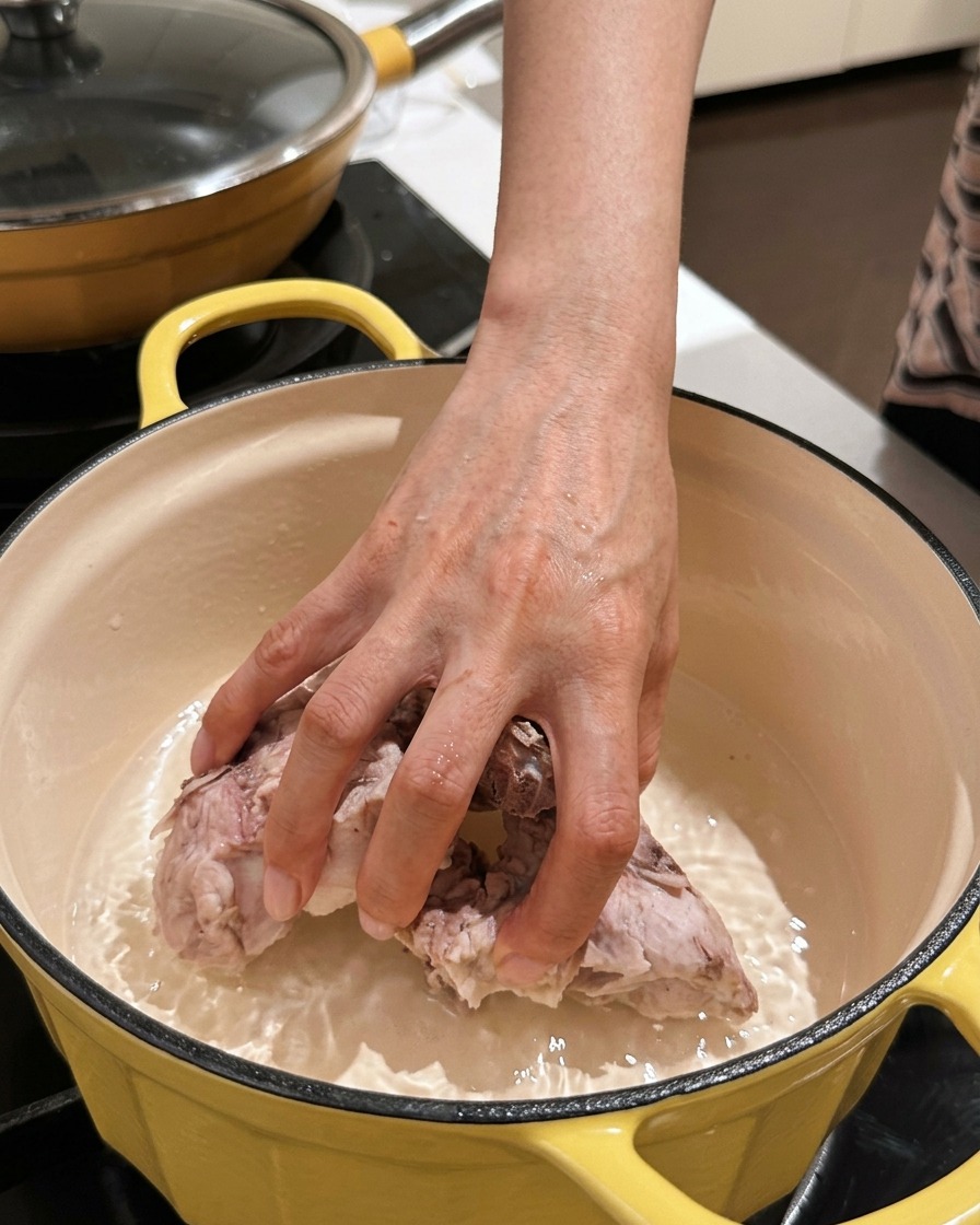 Una mano colocando trozos limpios de espinazo de cerdo de nuevo en una olla de cocción vacía.
