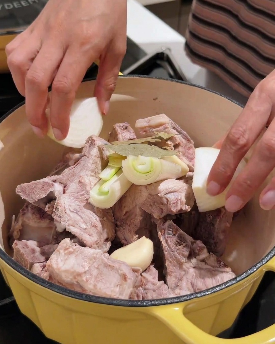 Varios aromáticos incluyendo ajo, cebolla y pasta de soja siendo añadidos a la olla con cerdo.