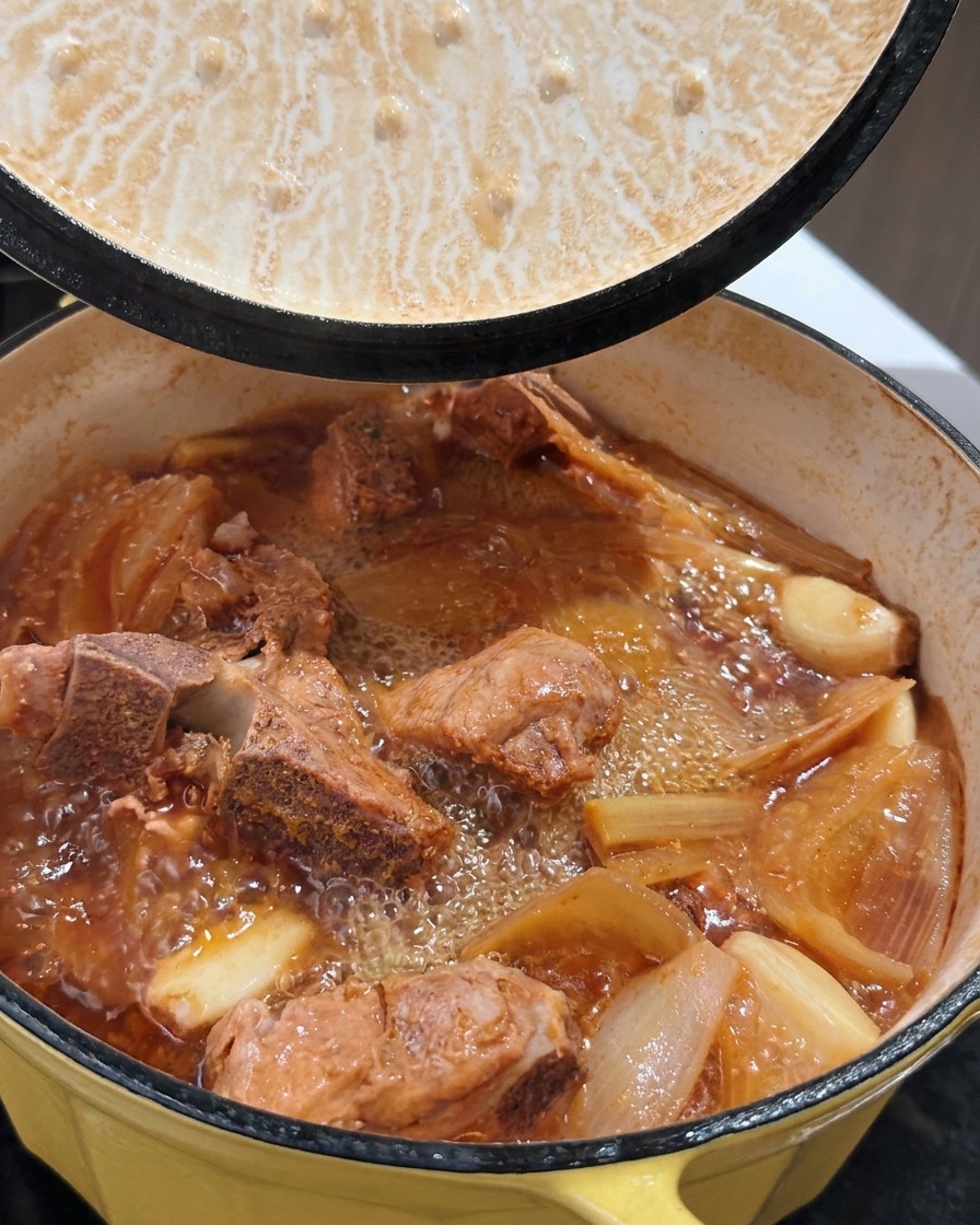 Una olla de costillas de cerdo estofadas burbujeantes con caldo rico mientras se levanta la tapa.