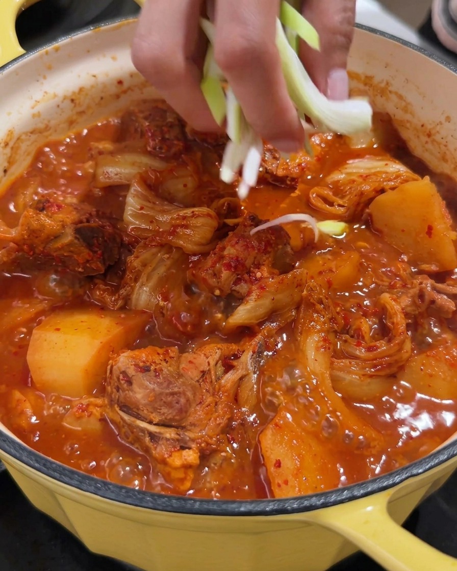 Una olla vibrante de sopa picante de espinazo de cerdo siendo adornada con cebollines picados frescos.