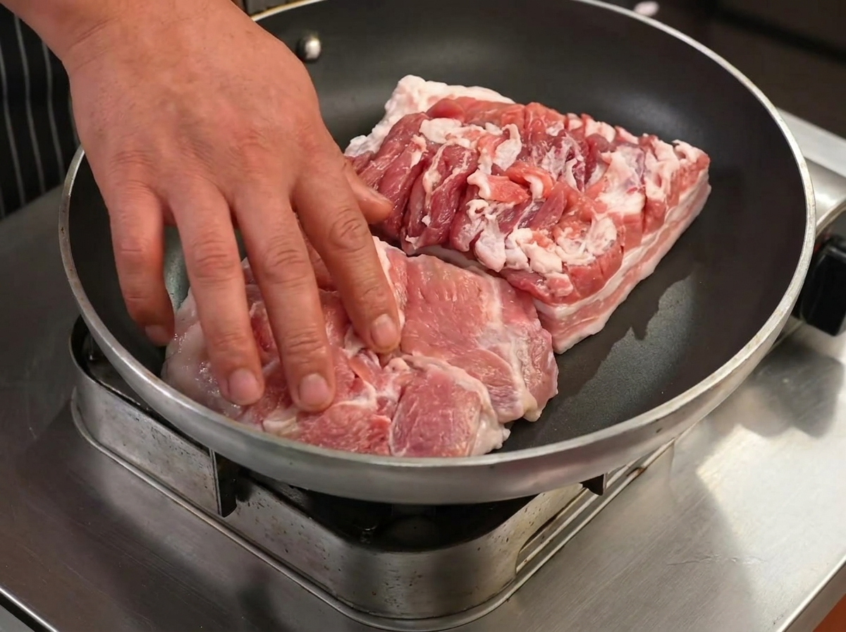 Rebanadas de panceta friéndose en una sartén seca, comenzando a dorarse y soltar grasa.