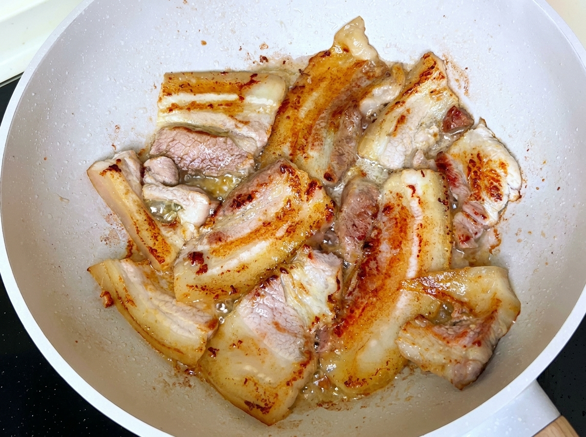 Rebanadas de panceta de cerdo friéndose y dorándose en una sartén con grasa derretida.