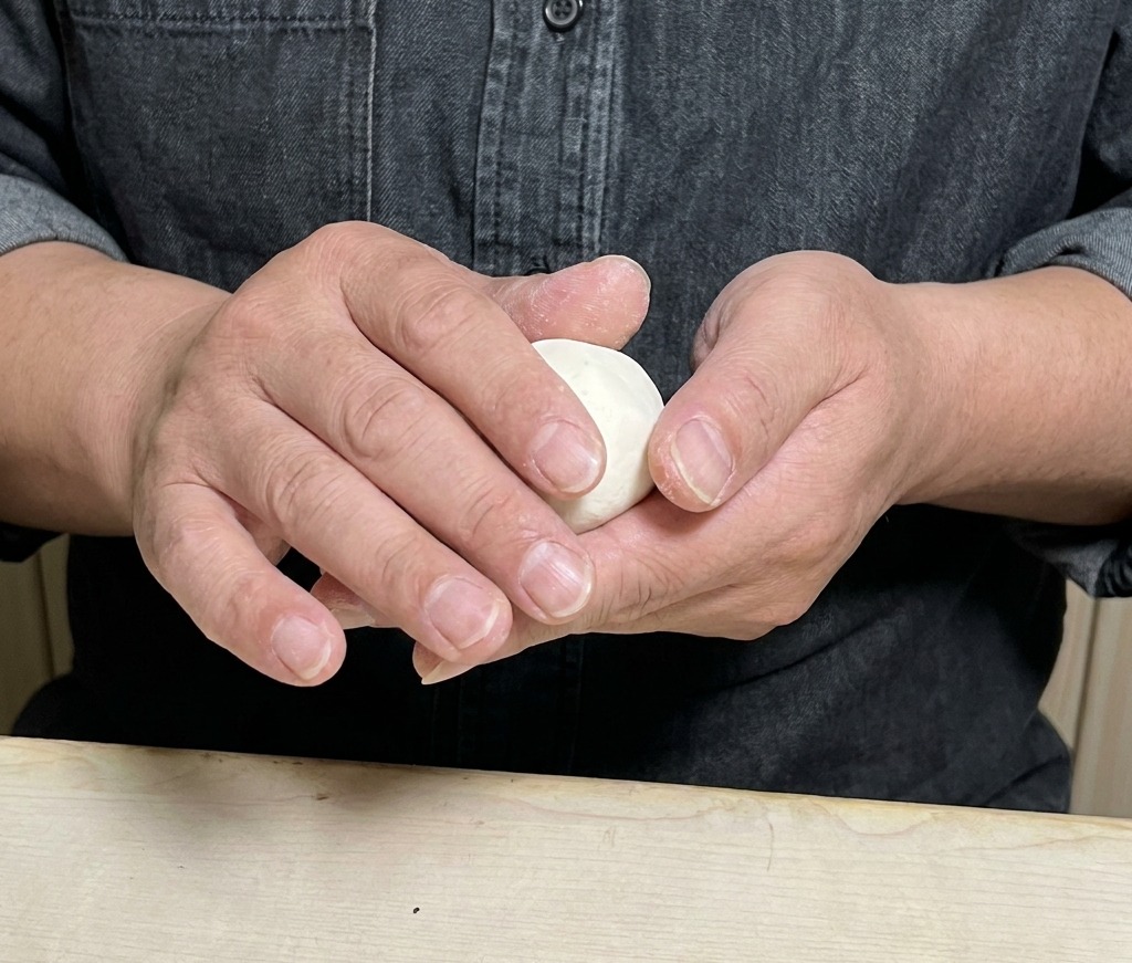 Manos doblando y sellando cuidadosamente una envoltura de masa redonda rellena con mezcla de carne.