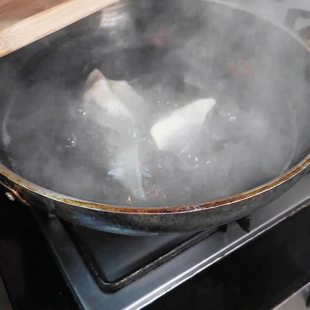 Varios dumplings sumergidos en una olla grande con agua hirviendo, con vapor elevándose desde la olla.