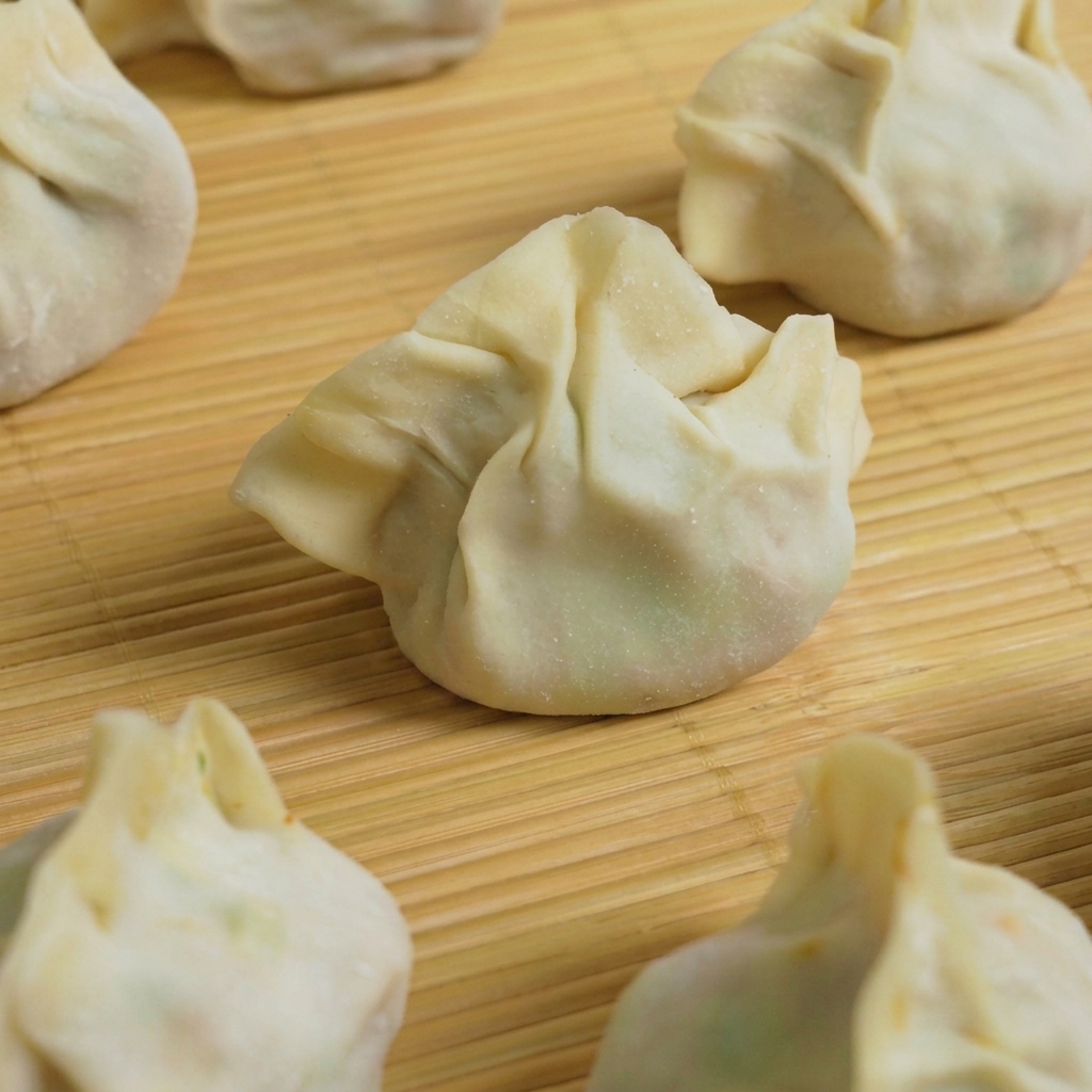 Varios dumplings armados sumergiéndose en una olla de agua hirviendo.