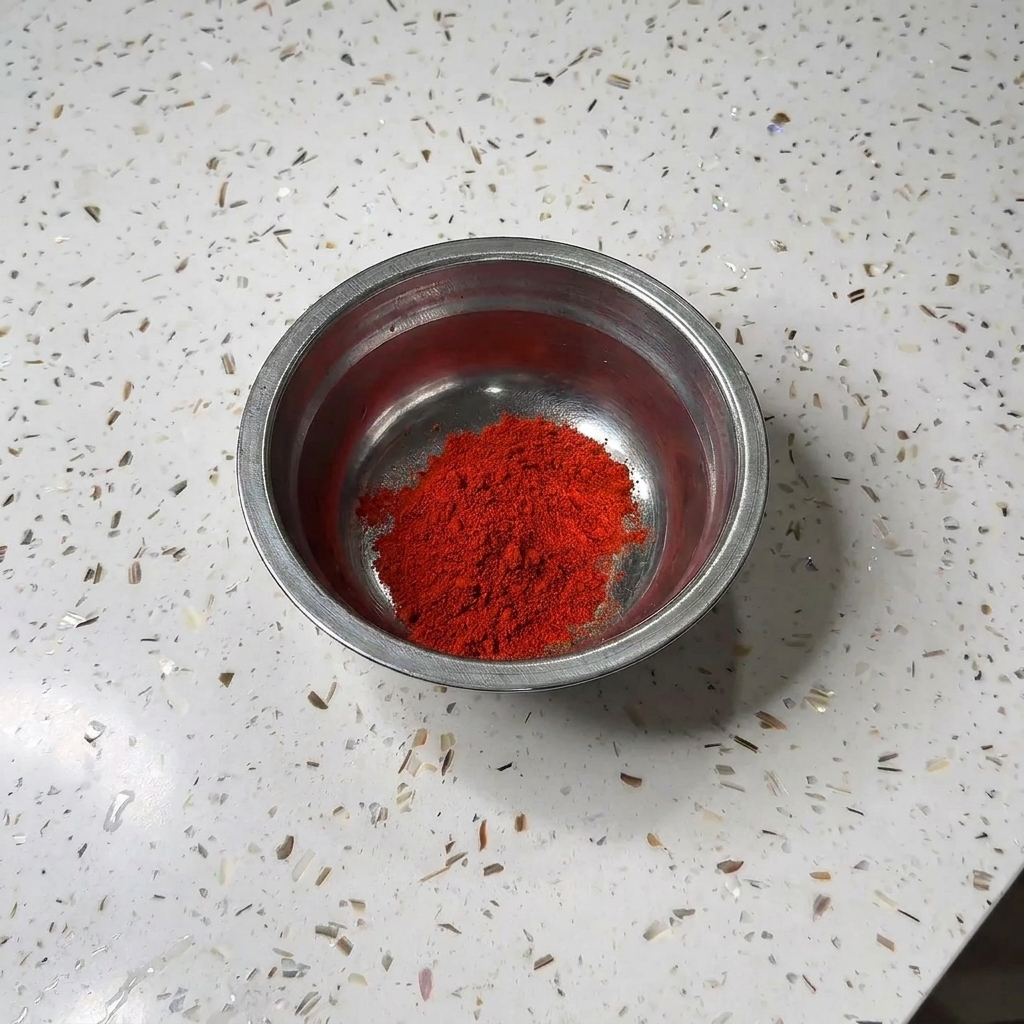 Un tazón pequeño de metal que contiene un montón de chile en polvo rojo y azúcar blanca sobre una encimera de granito.