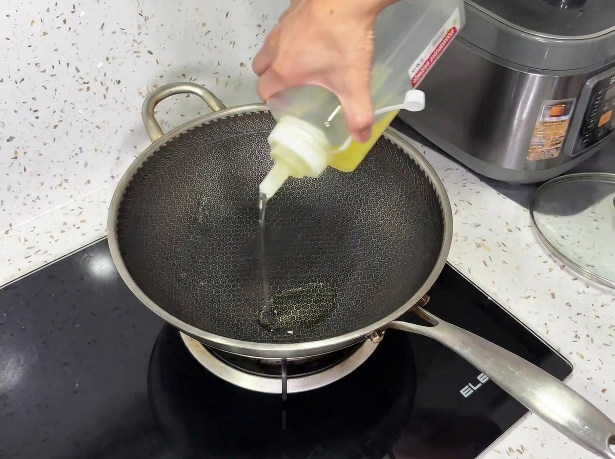 Aceite de cocina siendo vertido desde una botella exprimible en un wok de metal texturizado sobre una encimera de inducción negra.
