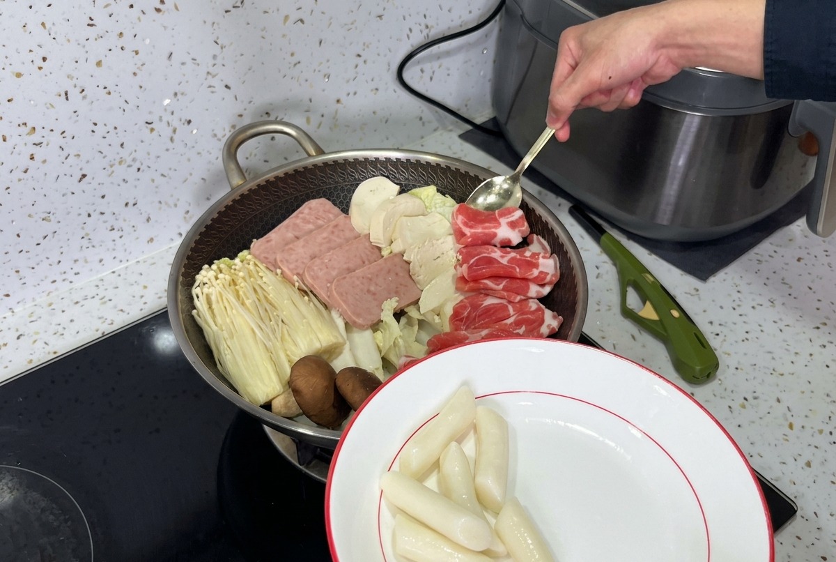 Una olla maravillosamente organizada de estofado militar coreano, con capas de carne en lata, champiñones, tofu y kimchi fresco listo para el caldo.