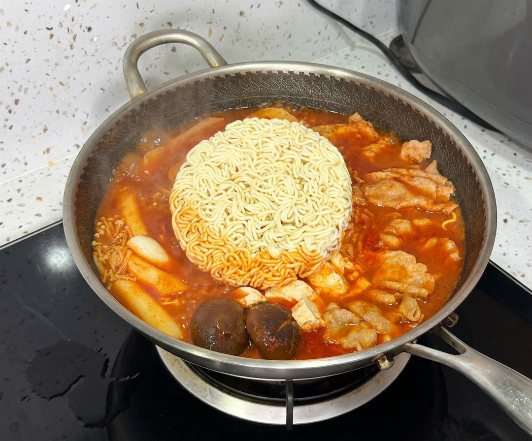Un bloque de fideos ramen cociéndose en el centro del vibrante y burbujeante estofado militar coreano.