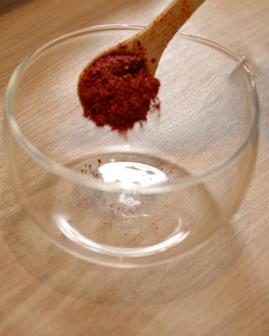 Chile en polvo en un bol de cristal con salsa picante coreana y salsa de soja ligera siendo añadidas.