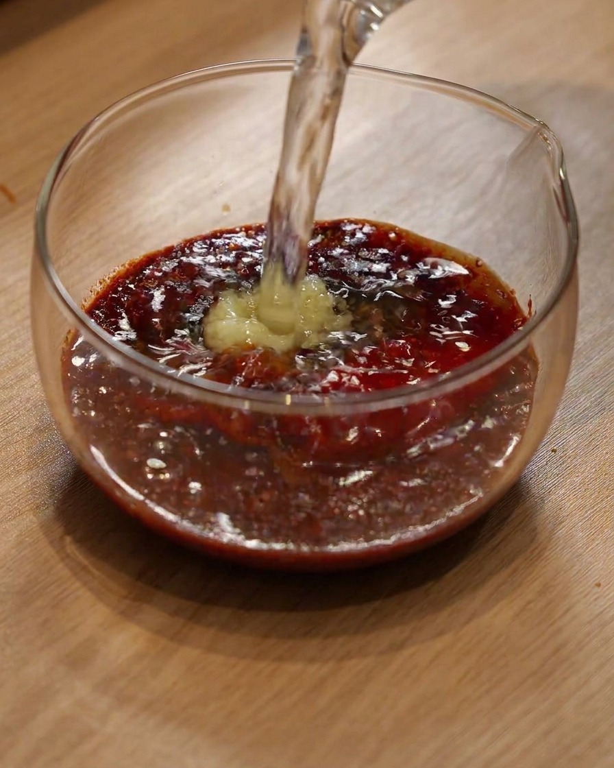 Agua siendo vertida en un bol de cristal con chile en polvo y condimentos.