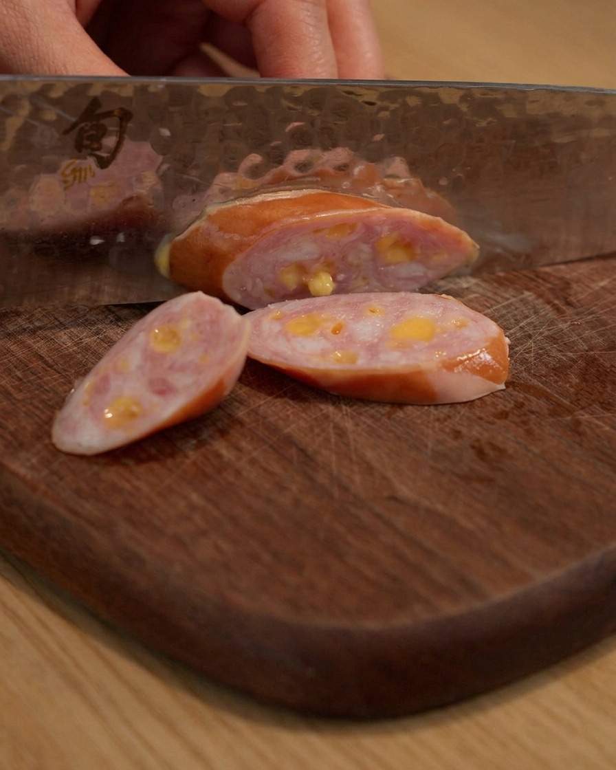 Salchicha siendo cortada en trozos sobre una tabla de cortar de madera.