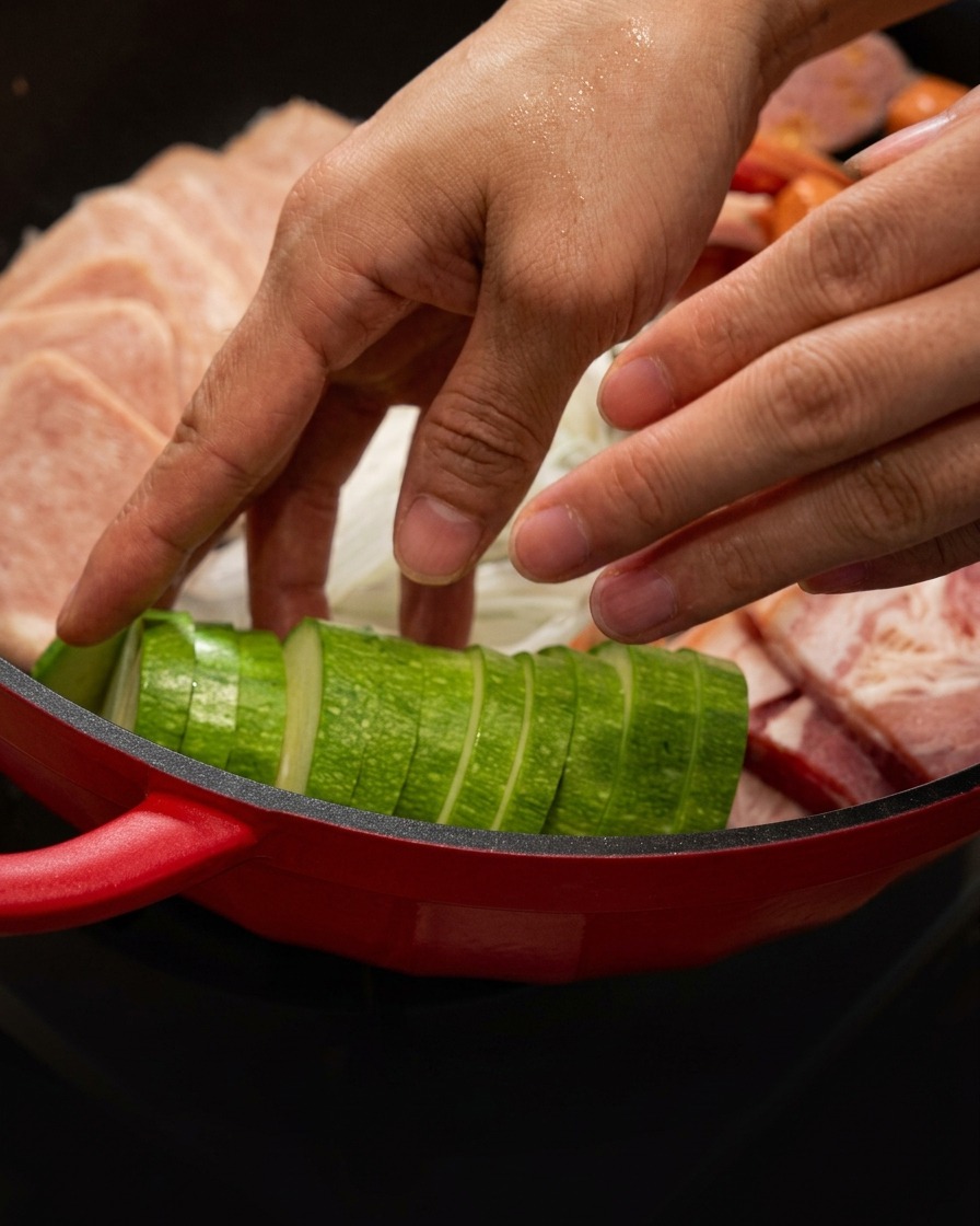 Rodajas de calabacín siendo colocadas ordenadamente en la olla roja junto a la carne.
