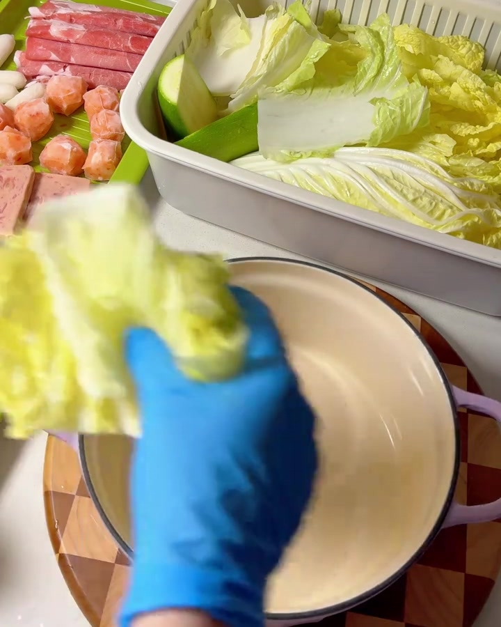 Manos con guantes colocando hojas de col napa en una olla morada.