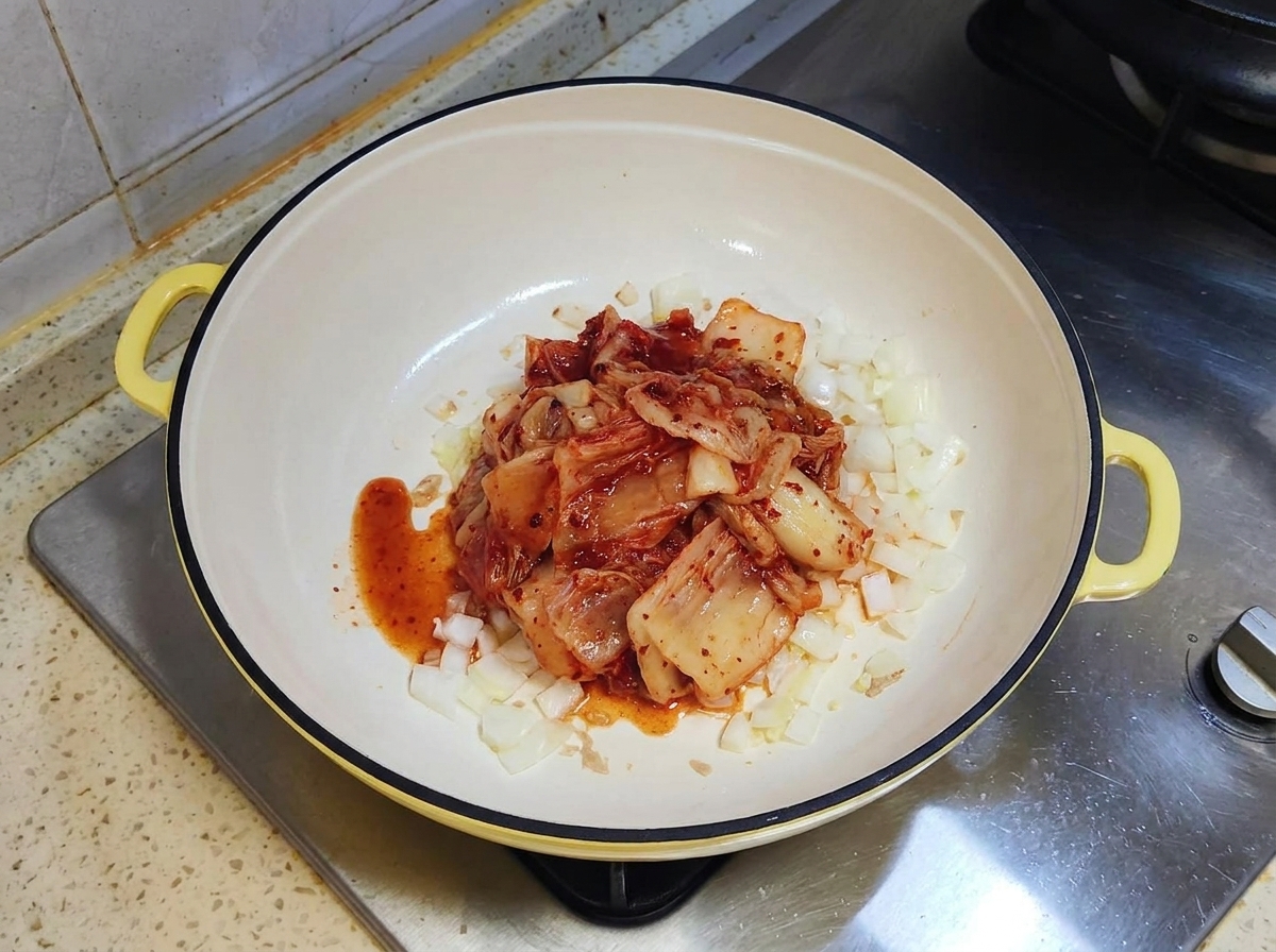 Una porción de kimchi fermentado rojo sentado encima de cebollas salteadas en una sartén blanca.
