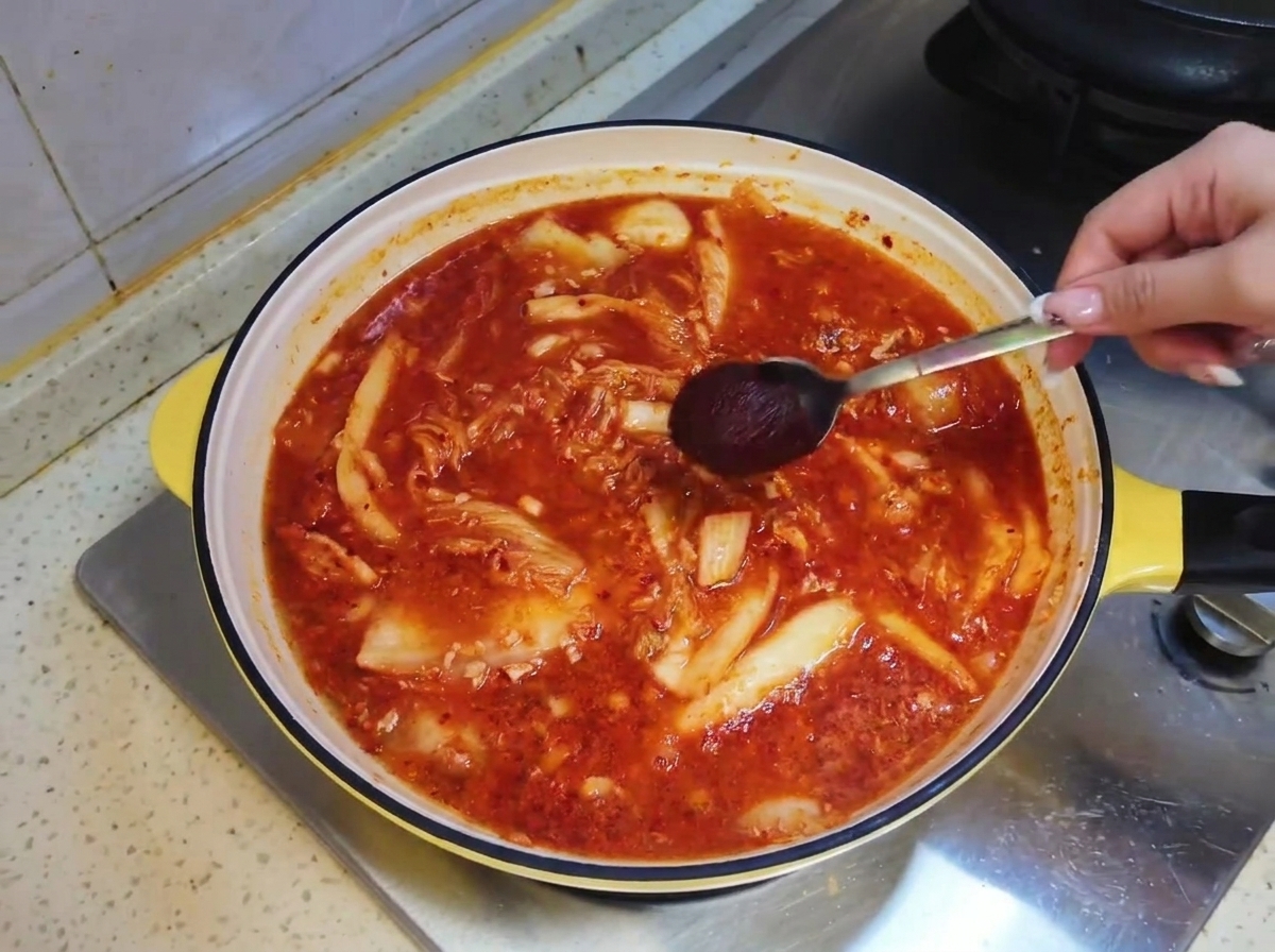 Una cucharada de salsa picante coreana siendo bajada en el caldo de sopa rojizo dentro de la sartén.