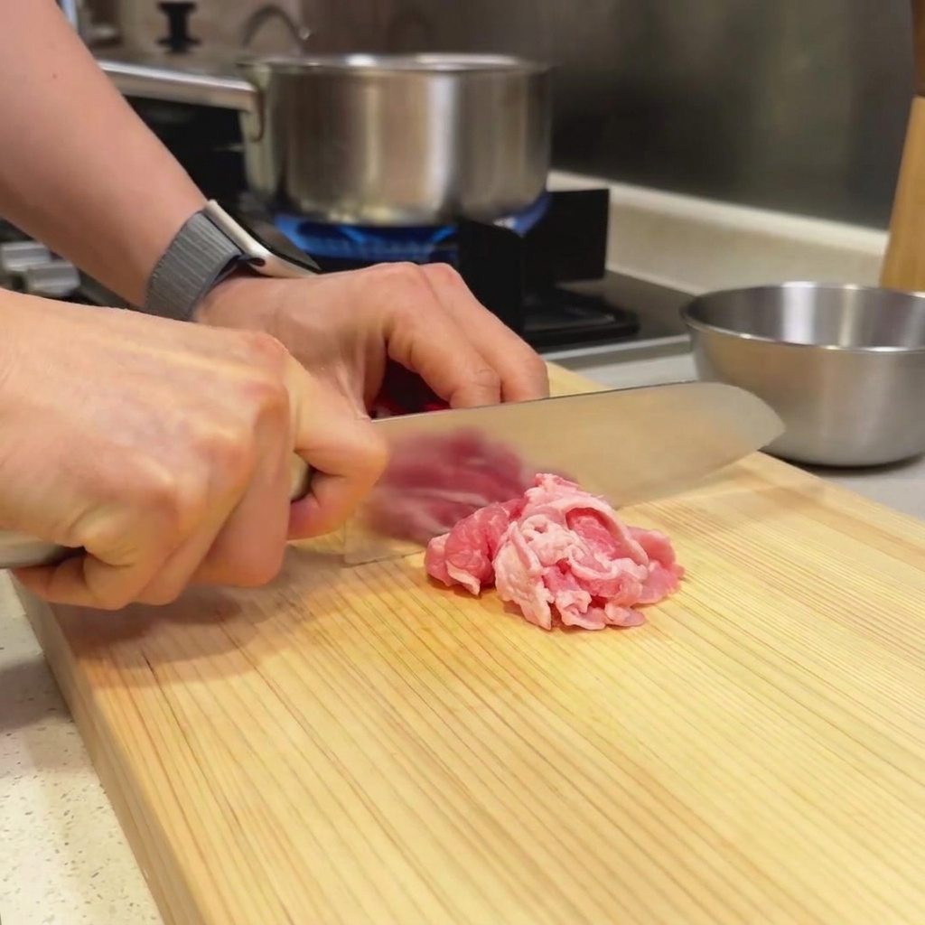 Finas rodajas de ternera reposando en una tabla de cortar de madera siendo preparadas con un cuchillo de chef.