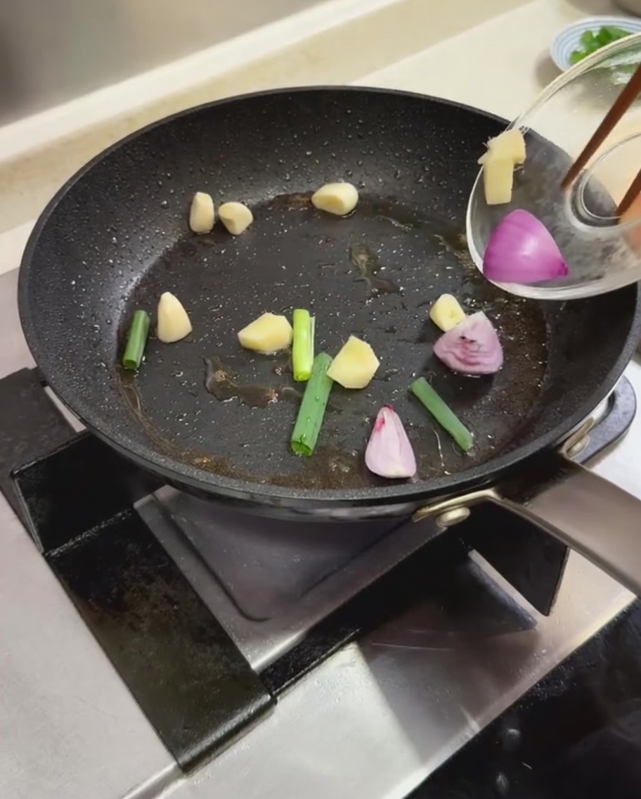 Trozos de cebollino, dientes de ajo y cebollas rojas en rodajas siendo salteados en una sartén caliente.