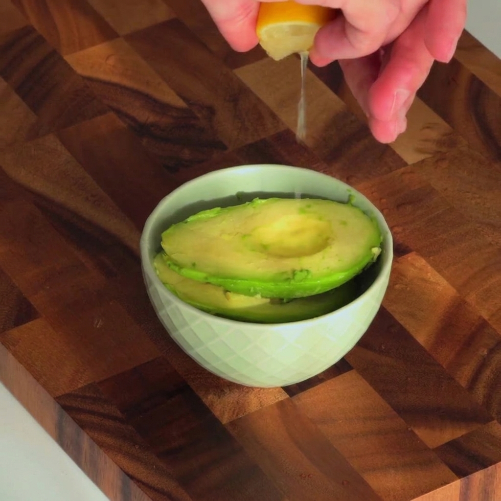 Jugo de limón fresco siendo exprimido en un tazón pequeño que contiene la pulpa del aguacate.