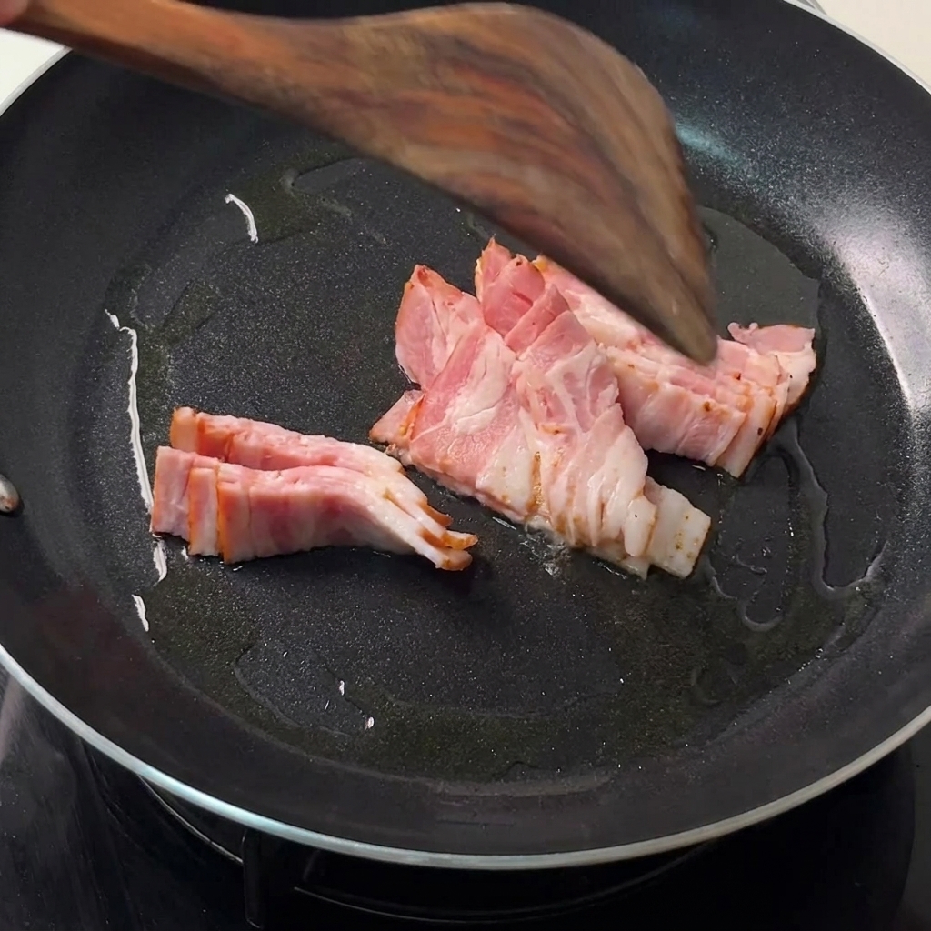 Tiras de tocino friéndose en una sartén negra caliente con una espátula de madera dándoles la vuelta.