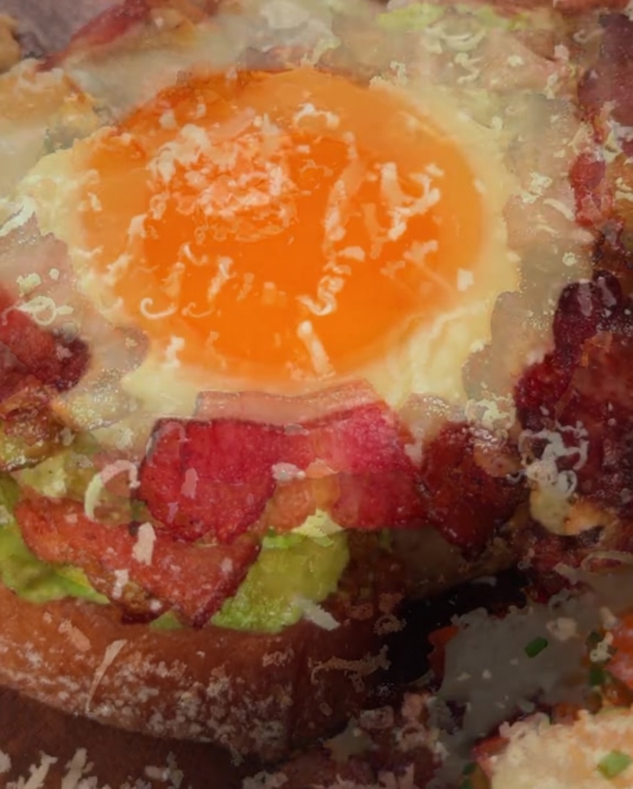 Queso parmesano rallado siendo espolvoreado sobre la parte superior de un sándwich completo de aguacate y huevo.