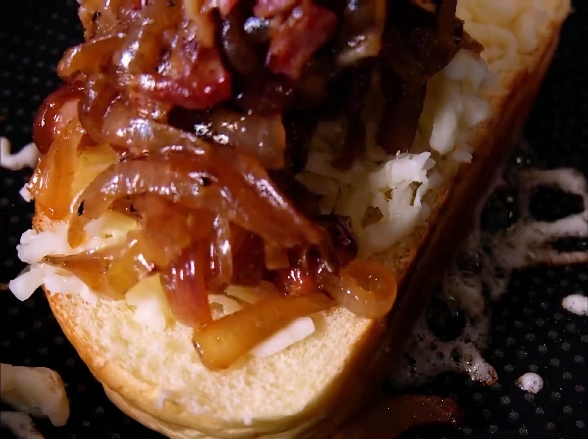 Una pila generosa de cebollas caramelizadas y trozos de tocino sobre queso rallado en una rebanada de pan.