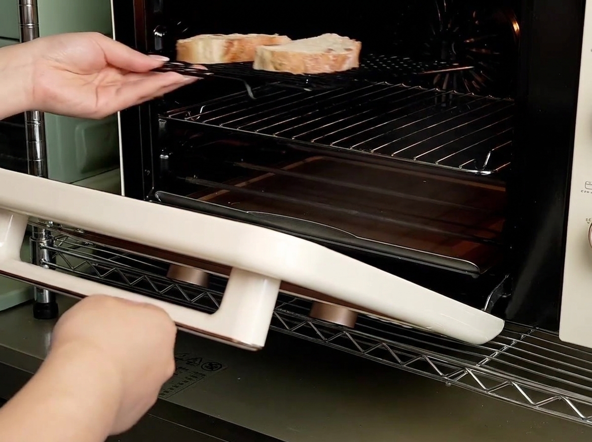 Manos deslizando una rejilla con dos rebanadas de pan en un pequeño horno de convección.