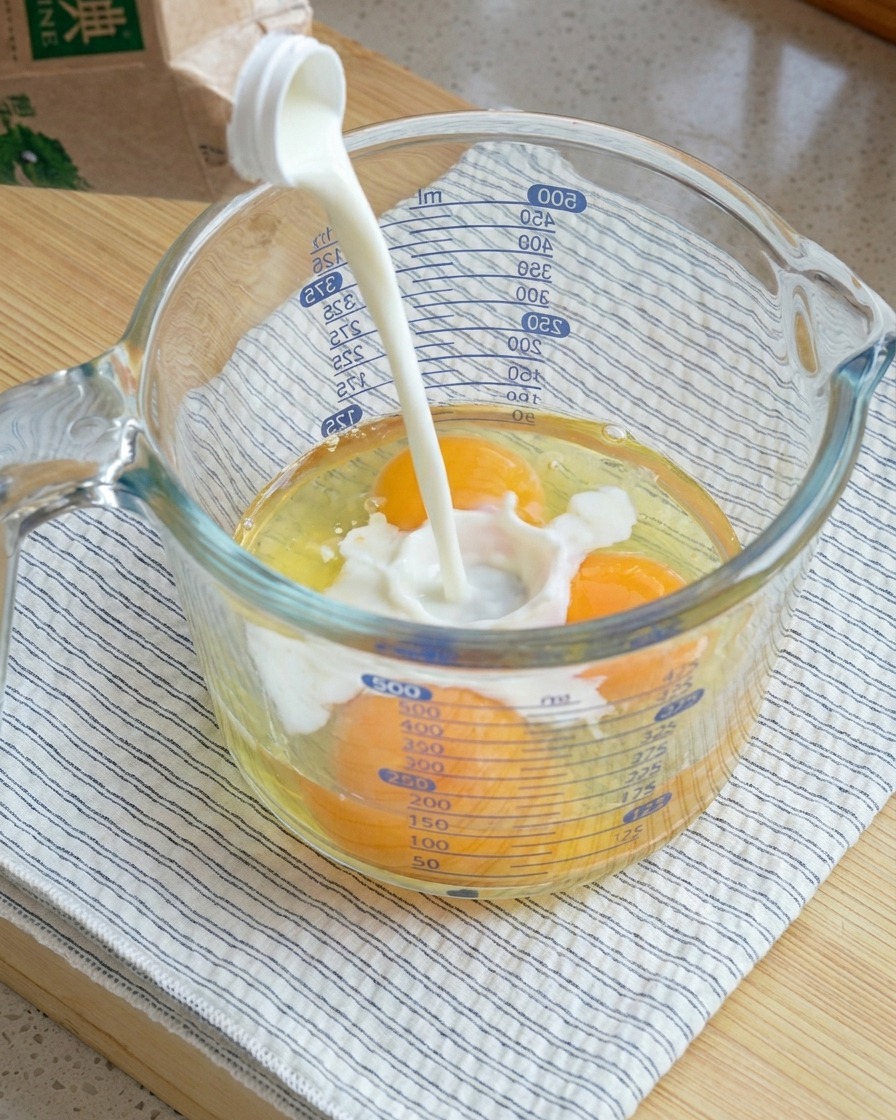 Vertiendo leche en una taza medidora de vidrio grande que contiene tres huevos crudos.