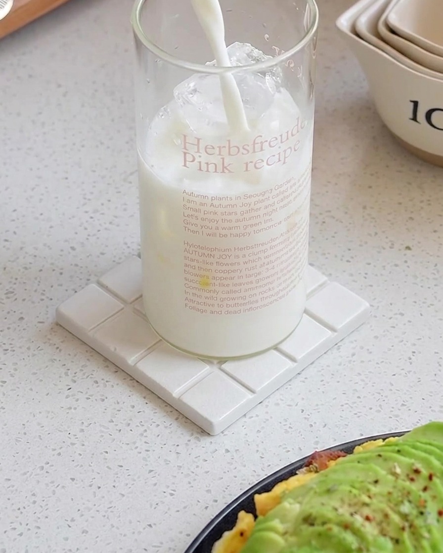 Leche vertida en un vaso alto lleno de cubitos de hielo sobre un posavasos blanco.
