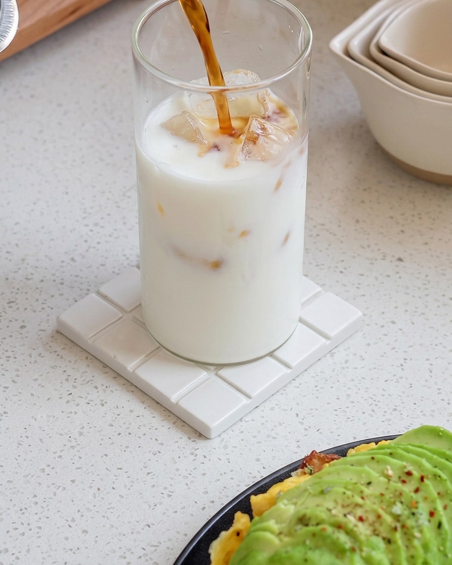 Espresso recién hecho siendo vertido en un vaso de leche helada, creando un patrón de gradiente arremolinado.