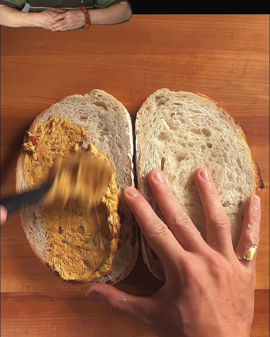 Rebanadas de pan rústico de masa madre con un aderezo siendo esparcido con una cuchara.