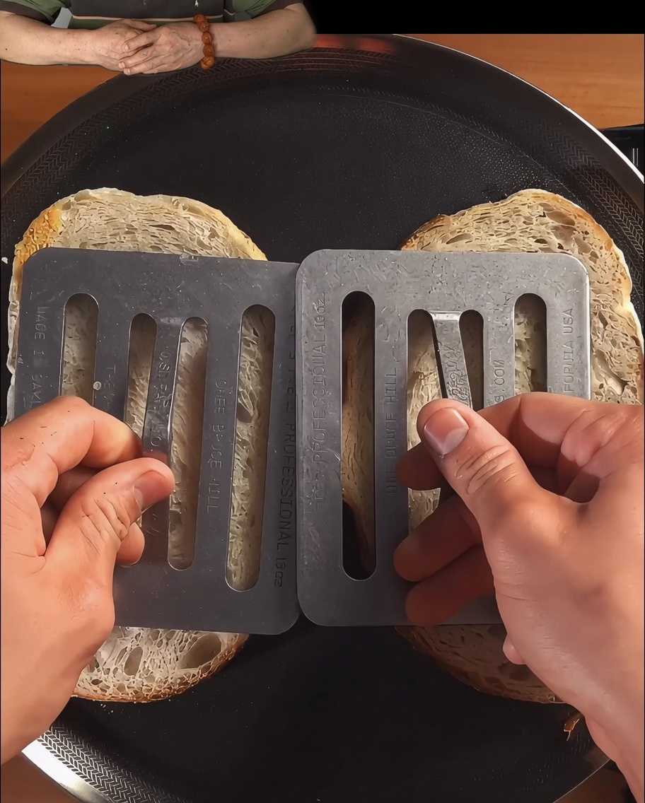 Rebanadas de pan siendo presionadas y tostadas en una sartén negra hasta que estén doradas.