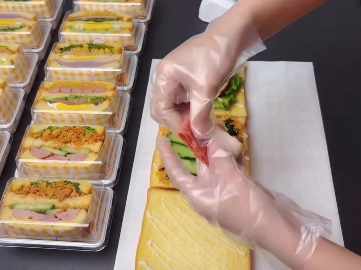 Manos con guantes sosteniendo y organizando pequeñas secciones de tocino cocido para colocar en la construcción del sándwich.