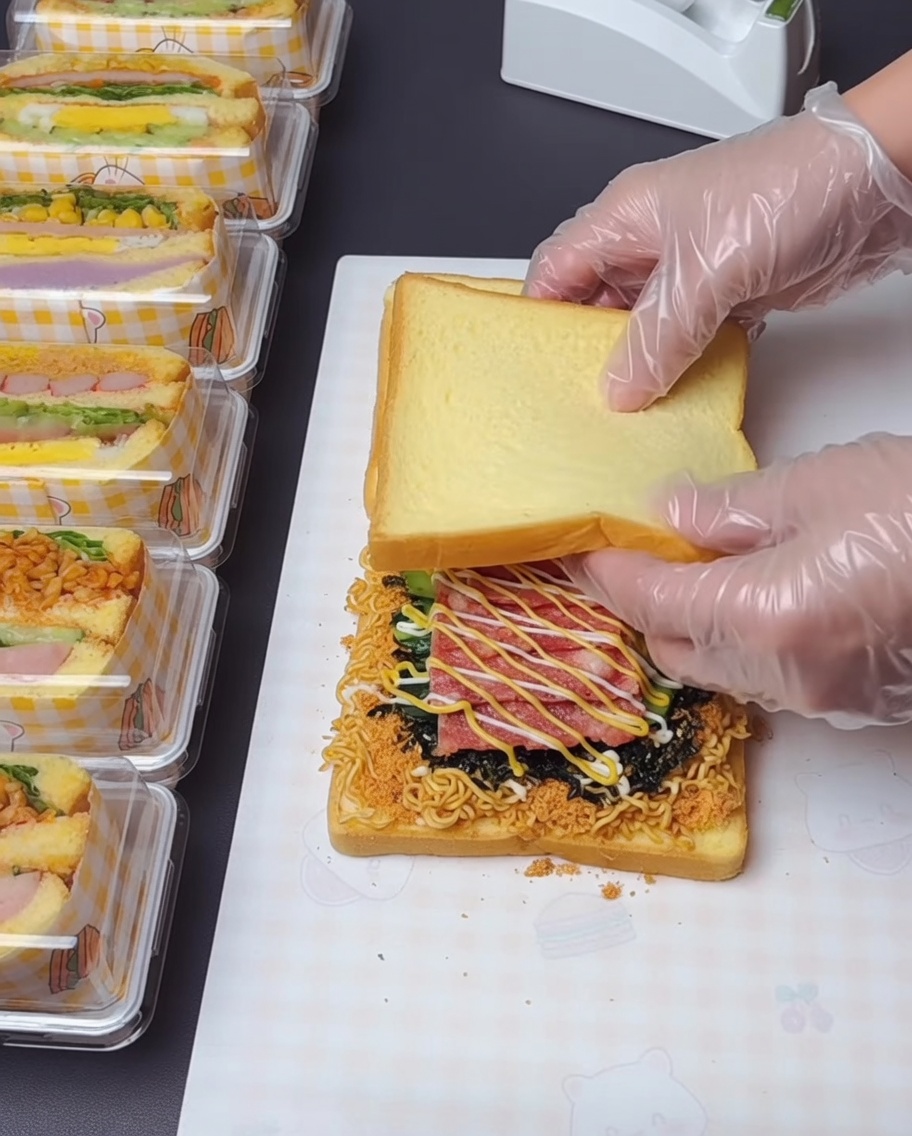 Un par de manos con guantes levantando y apilando la rebanada superior de tostada sobre las capas cargadas debajo.