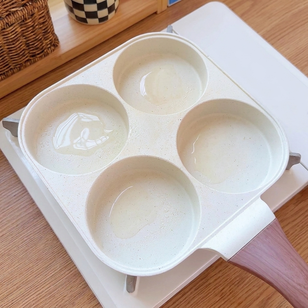 Huevos siendo vertidos en los compartimentos engrasados de una sartén de múltiples tazas.