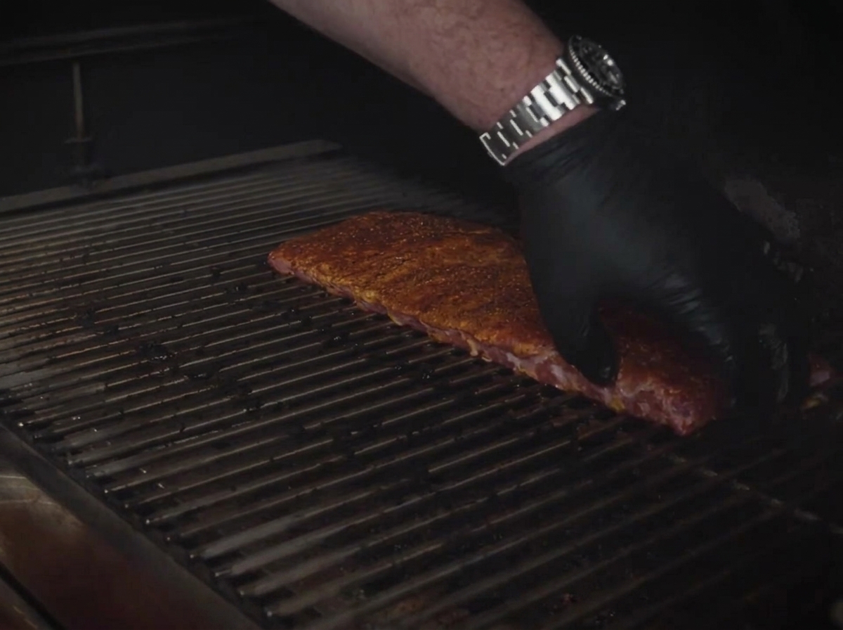 Costillas sazonadas colocadas de forma plana sobre las parrillas metálicas de un ahumador.