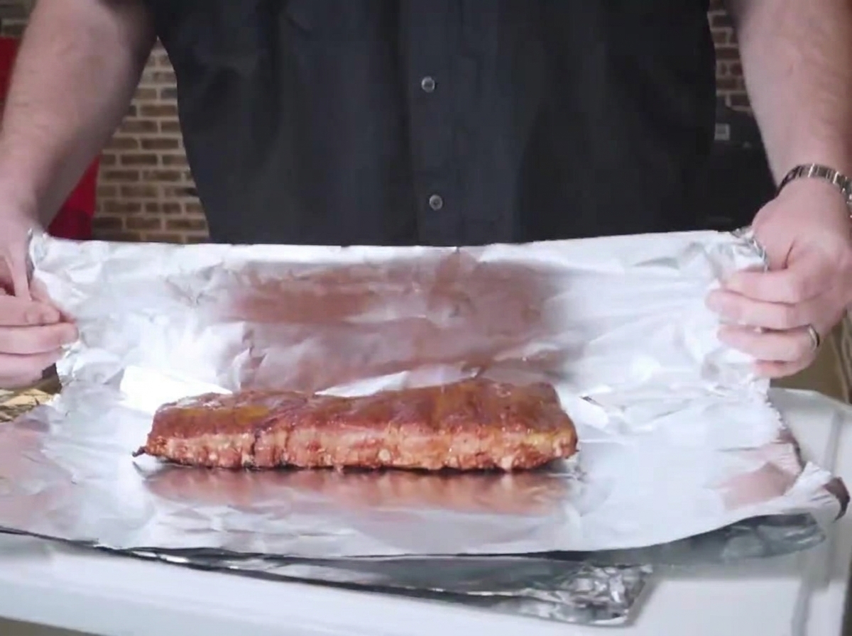 Costillas ahumadas colocadas sobre una hoja de papel de aluminio, listas para envolverse firmemente con el lado de los huesos hacia abajo.