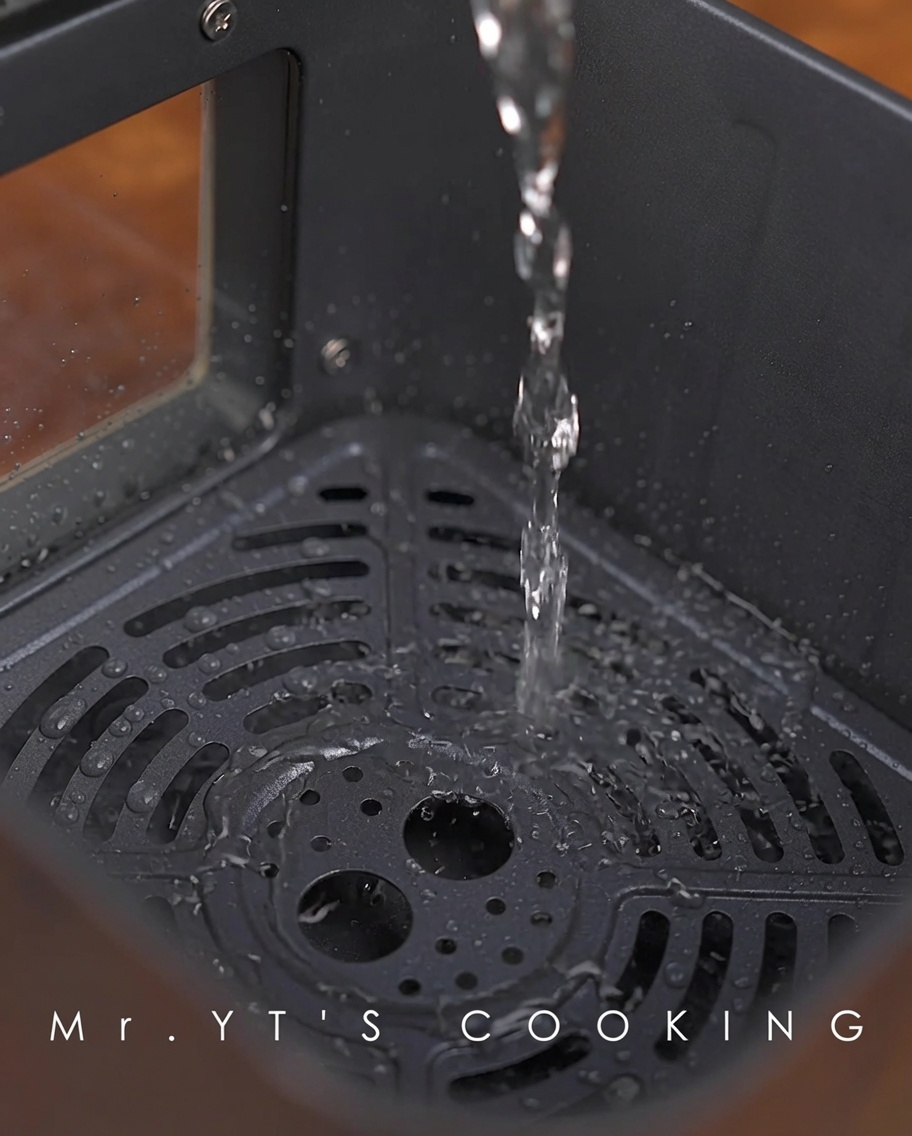 Agua siendo vertida en el fondo de la cesta de la air fryer.