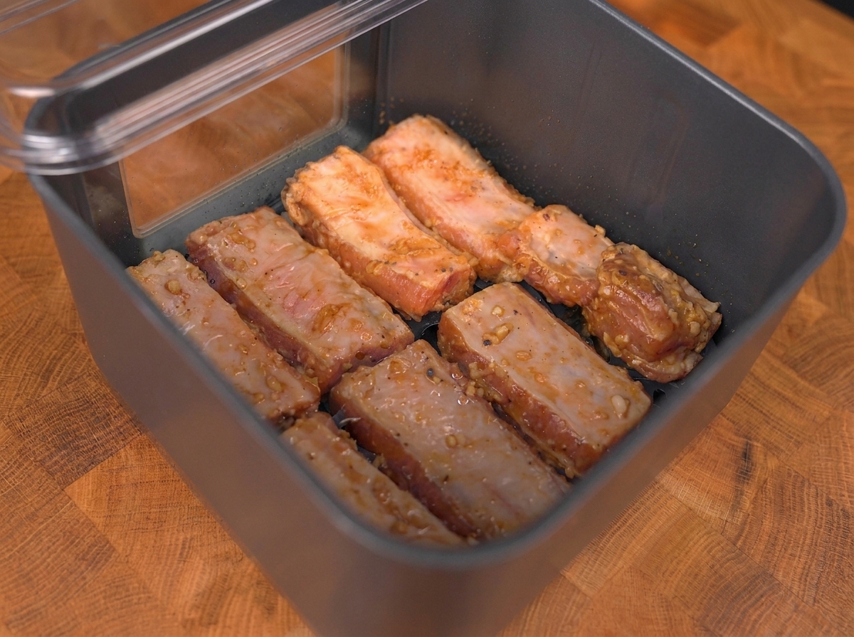 Costillas de cerdo marinadas dispuestas en una sola capa dentro de la cesta de la air fryer.