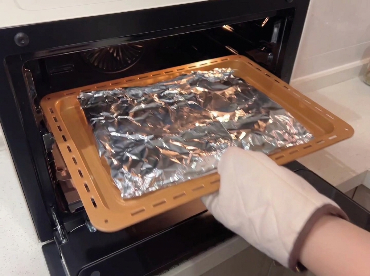 Una persona usando un guante de horno protector colocando una bandeja para hornear con costillas envueltas en papel de aluminio en un horno de convección.