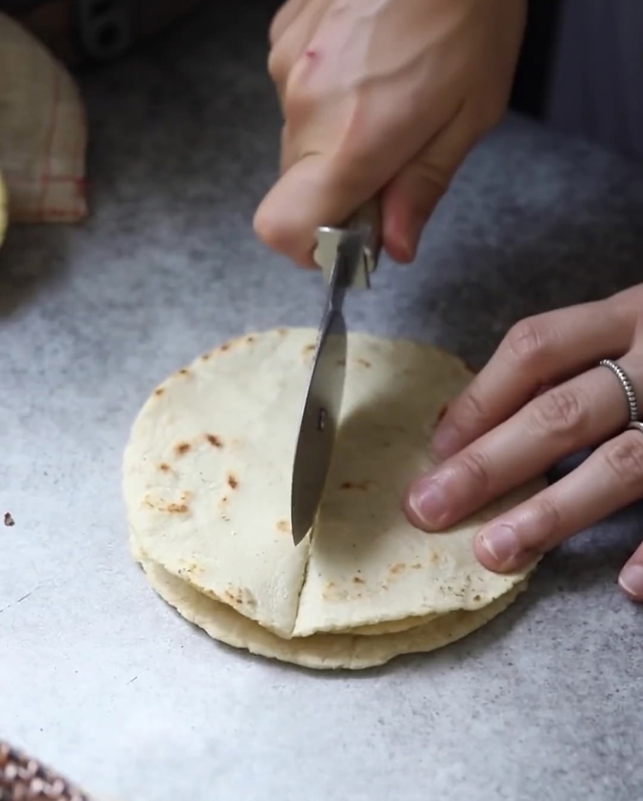 Tortillas planas y cocidas apiladas siendo cortadas en secciones triangulares con una cuchilla.