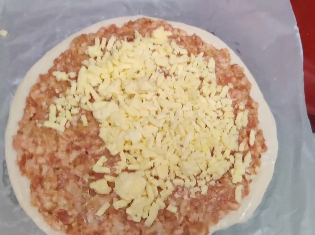 Queso amarillo rallado amontonado sobre una capa de carne picada cruda en un panqueque de cebollino.