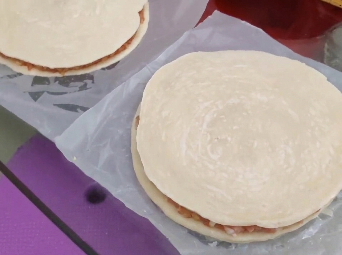 Un segundo panqueque de cebollino redondo colocándose sobre el relleno de carne y queso para formar un pastel cerrado.
