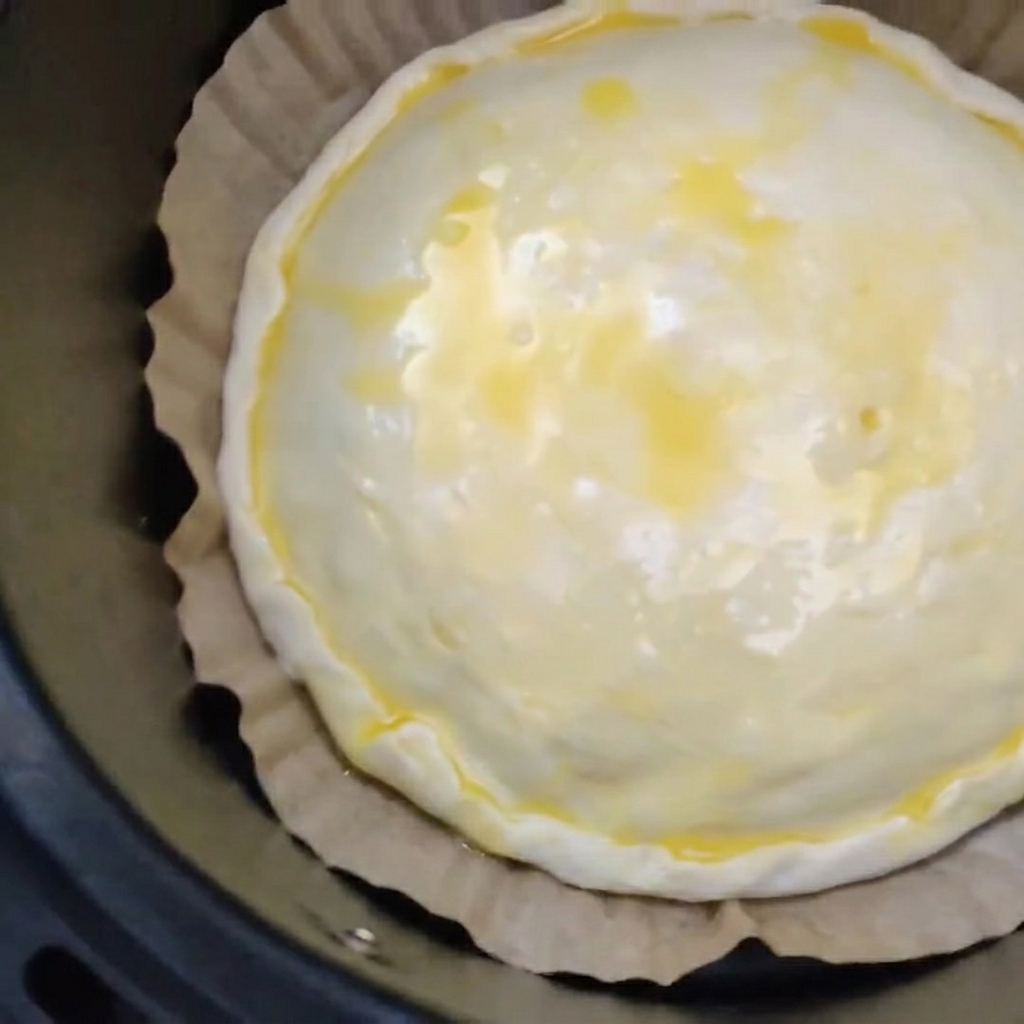 Un pastel de carne y queso sin hornear con la parte superior untada con huevo sobre papel pergamino marrón dentro de una cesta de freidora de aire negra.