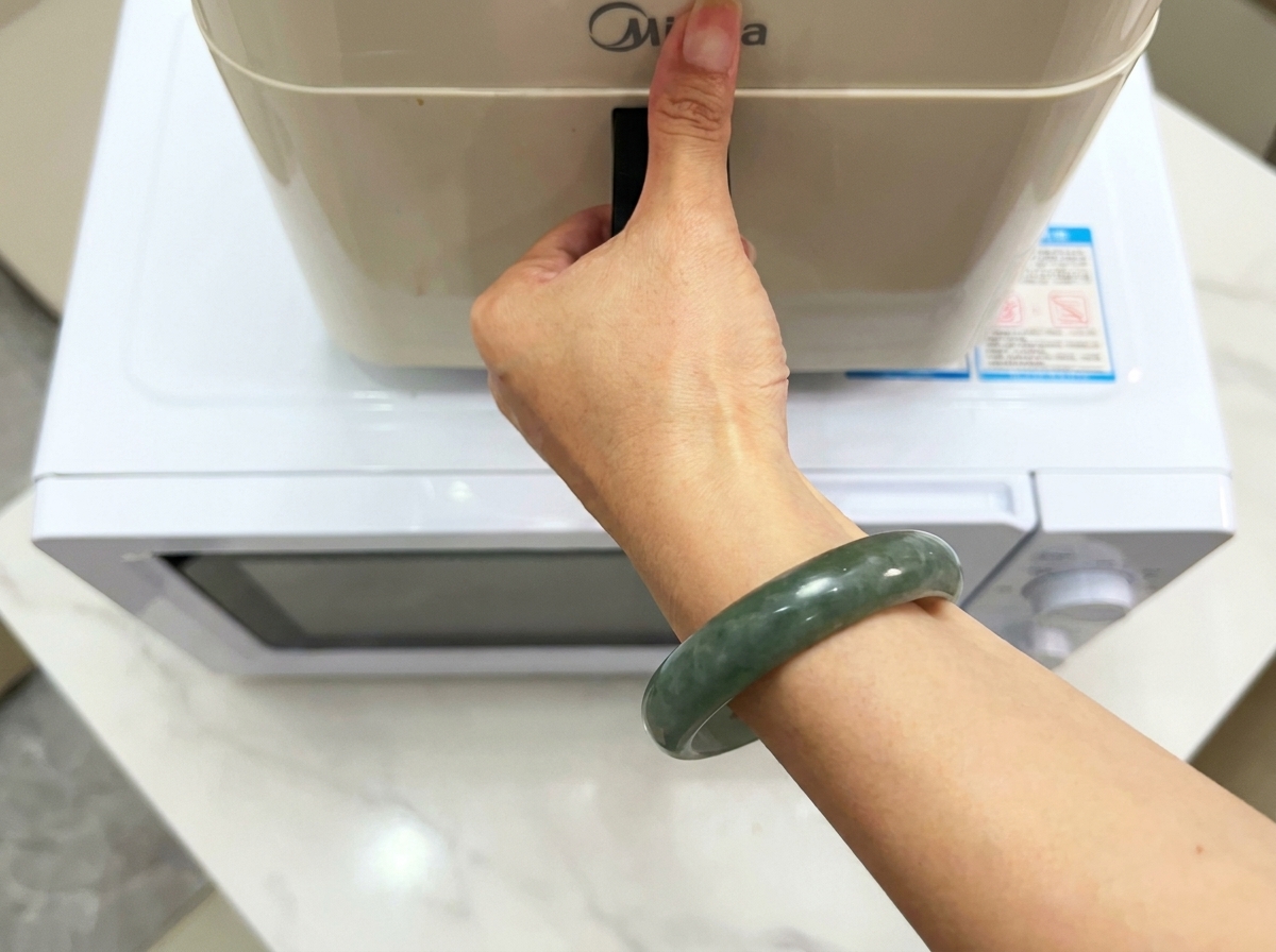 Una mano sosteniendo la manija de un electrodoméstico de cocina moderno sentado en una superficie blanca.
